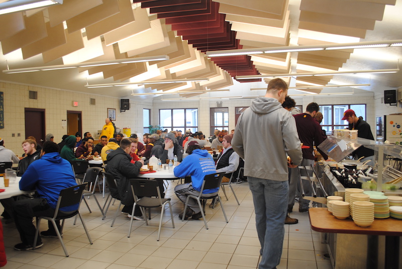 A large group of men enjoy lunch in the dining hall after volunteering with the youth of Eagle Village
