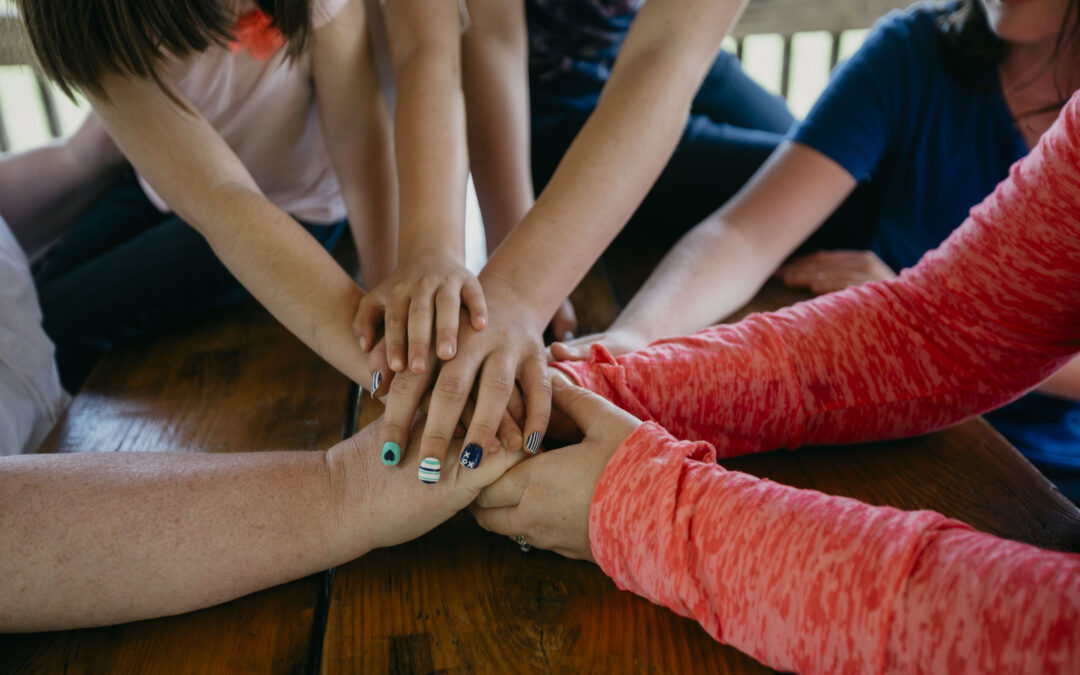 A family piles all their hands in the center of the picnic table