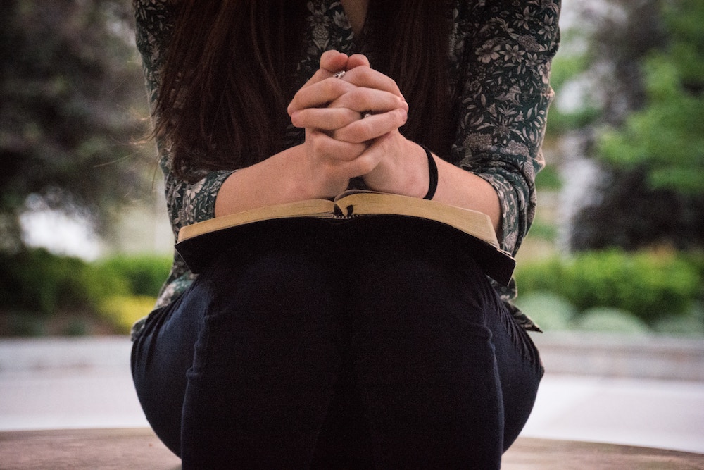 A woman folds her hands over her Bible to pray